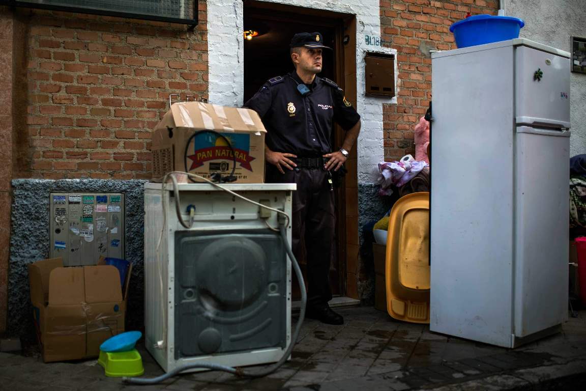 Police block the apartment's entrance as Amalio Barrul Gimenez' belongings lay on the street after Amalio and his family's got evicted in Madrid, Spain, Tuesday, June 24, 2014. Amalio Barrul Gimenez, , 41 years old, his wife Isabel Morales Bachiller, 35 years old, 2 month pregnant, and three children live with a low income coming from selling goods in the street and state benefits of 530 euros ($720). They occupied Bankia Bank apartment one and a half year ago and have tried to negotiate to pay a low rent but the bank demanded their eviction. The eviction was carried out in spite of the Victims' Mortgage Platform (PAH). Banners read "Shame" "you are laughing and we are suffering", "three children in the street", "a pregnant woman evicted", "extra payment to evict people". (AP Photo/Andres Kudacki)